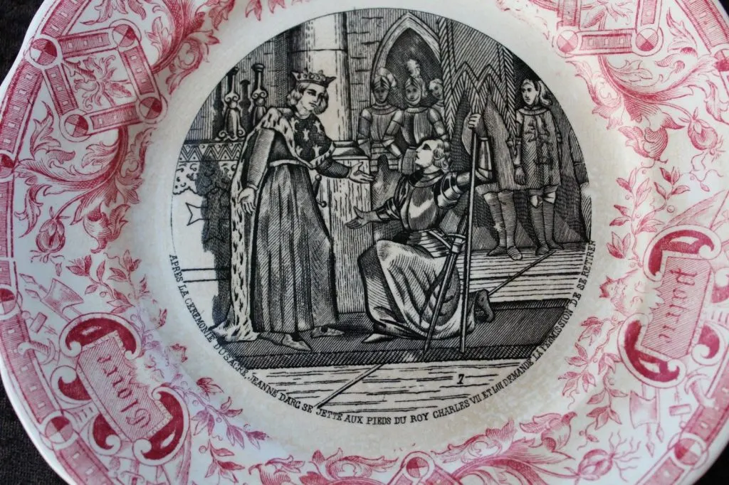 Assiette de faïence à décor imprimé en noir : Jeanne d'Arc aux pieds de Charles VII, bordure rose à rinceaux