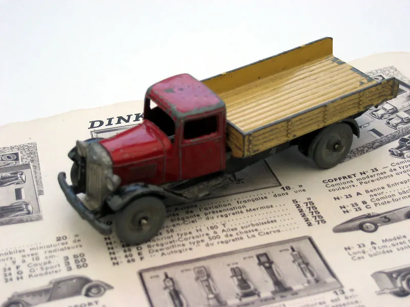 Camion plateau Dinky Toys rouge et beige de 1938 posé sur une page de catalogue ancien
