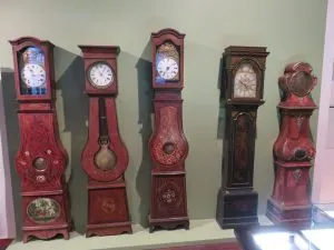 Cinq horloges comtoises à caisses peintes en rouge et brun alignées dans une vitrine de musée