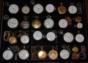 Collection de montres de poche anciennes à remontage manuel, boîtiers ouverts et savonnettes, rangées dans une vitrine
