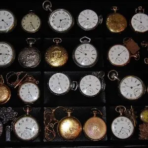 Collection de montres de poche anciennes à remontage manuel, boîtiers ouverts et savonnettes, rangées dans une vitrine