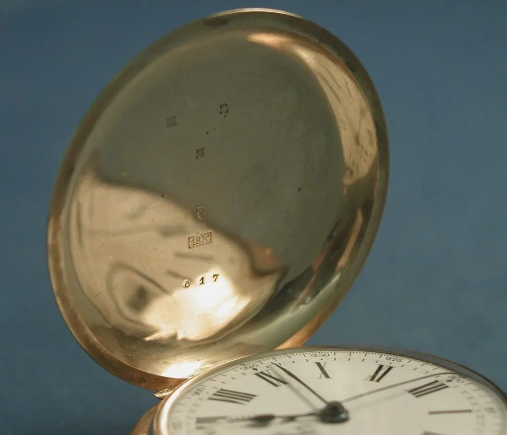Couvercle ouvert d'une montre de poche en or montrant de petits poinçons et un numéro frappés à l'intérieur