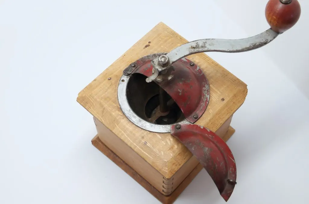 Dessus d'un moulin à café Peugeot cubique, couvercle rouge ouvert sur la trémie et la noix, manivelle