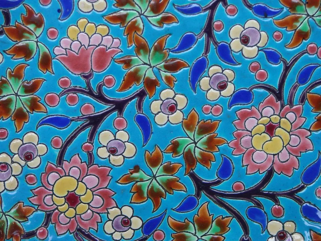 Détail d'émaux de Longwy : fleurs roses, jaunes et blanches cernées de noir sur fond bleu turquoise