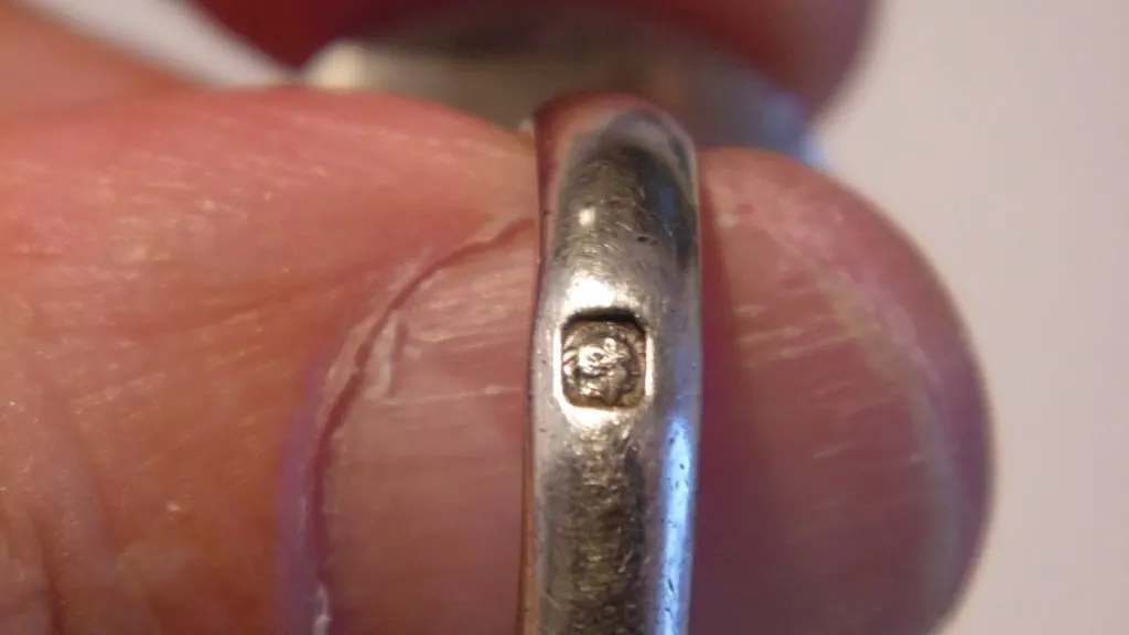 Gros plan d'un poinçon tête de Minerve frappé sur un petit objet en argent tenu entre deux doigts