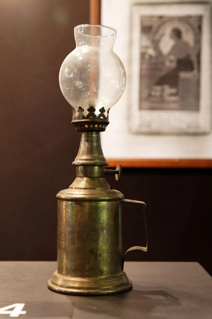 Lampe Pigeon en laiton doré avec globe de verre exposée devant une affiche ancienne