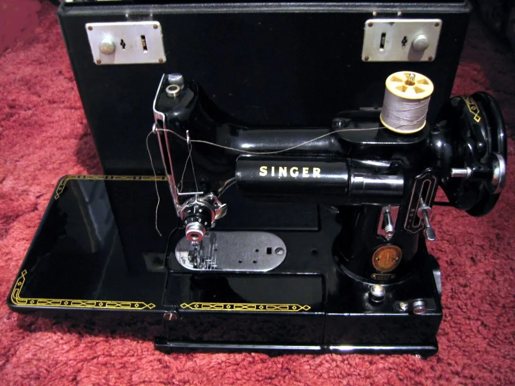 Machine à coudre portative Singer Featherweight 222K noire, avec bobine de fil, devant son coffret ouvert