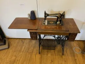 Machine à coudre Singer à pédale vers 1900, tête noire à décor doré posée sur sa table en bois et piétement en fonte