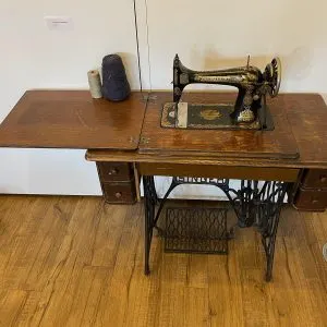 Machine à coudre Singer à pédale vers 1900, tête noire à décor doré posée sur sa table en bois et piétement en fonte