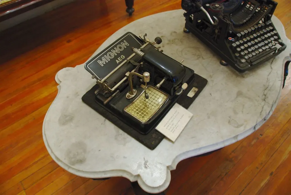 Machine à écrire à index Mignon AEG avec son pointeur et sa grille de lettres, posée sur une table en marbre