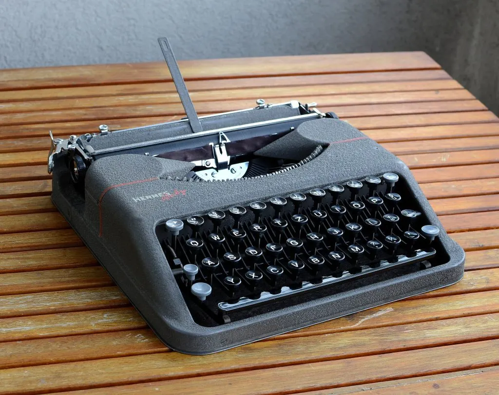 Machine à écrire portable Hermes Baby grise de 1948 posée sur une table en bois à lattes