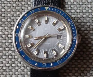Montre Lip Electronic ancienne à cadran argenté, guichet de date et lunette tournante bleue graduée