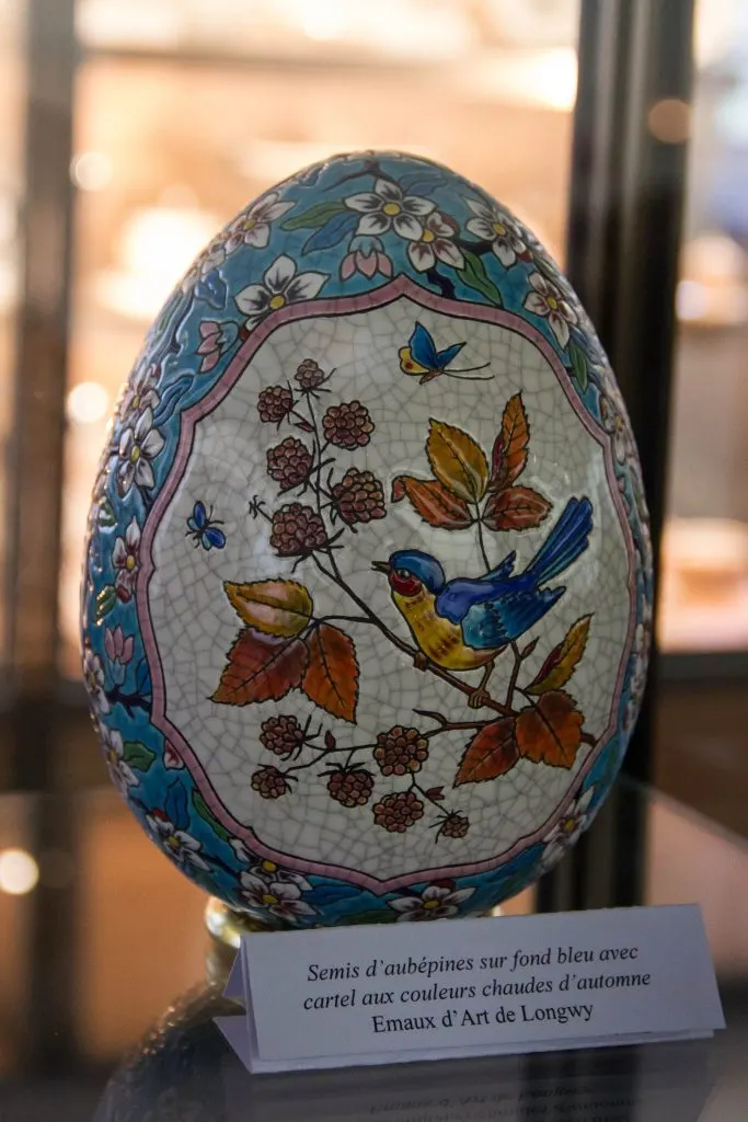 Œuf en émaux de Longwy à semis d'aubépines sur fond bleu, avec un cartel décoré d'un oiseau