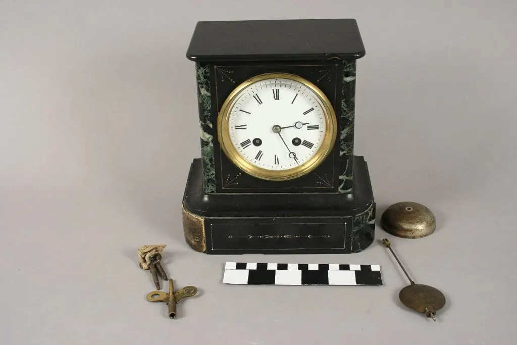 Pendule borne en marbre noir à cadran blanc, posée à côté de son balancier, de sa clé et de son timbre