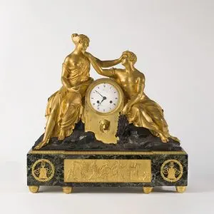 Pendule de cheminée dorée à deux figures féminines encadrant le cadran, sur un socle de marbre vert orné de bas-reliefs