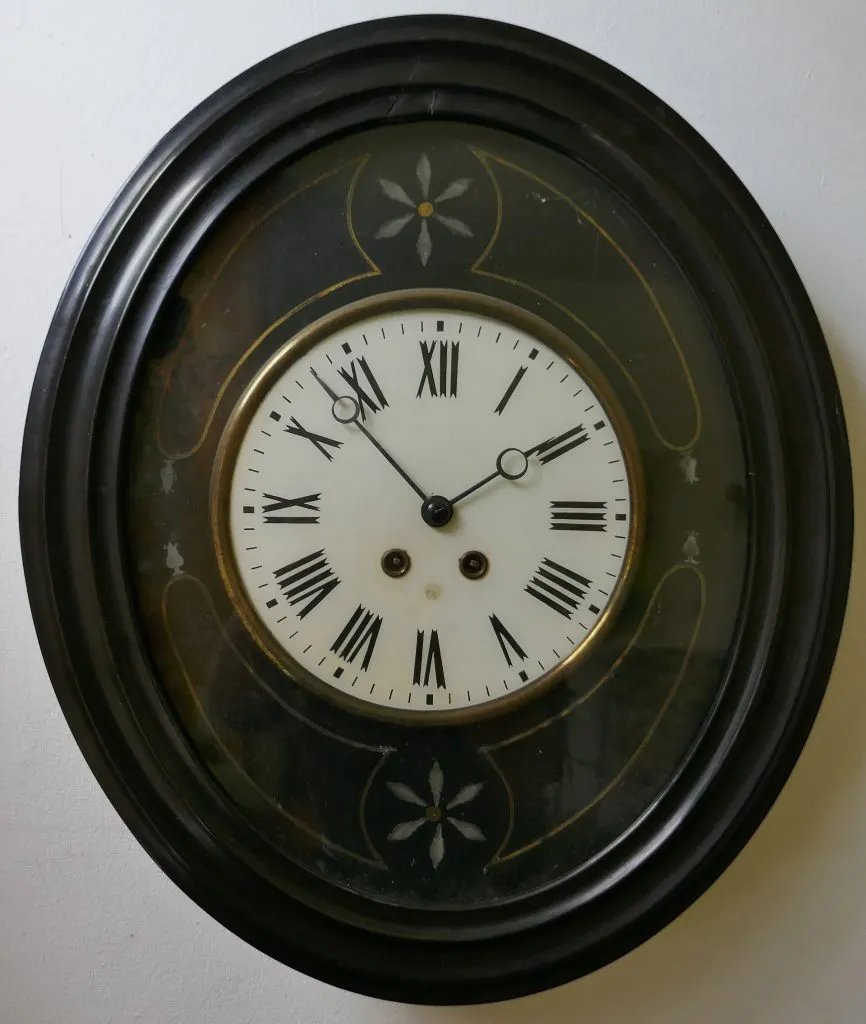 Pendule murale ovale à cadre noir mouluré, cadran émaillé blanc à chiffres romains et décor incrusté