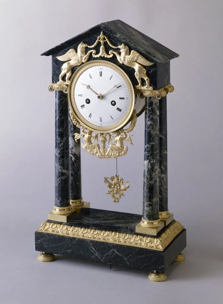 Pendule portique en marbre sombre à colonnes, cadran blanc et balancier doré, fronton orné de chimères dorées