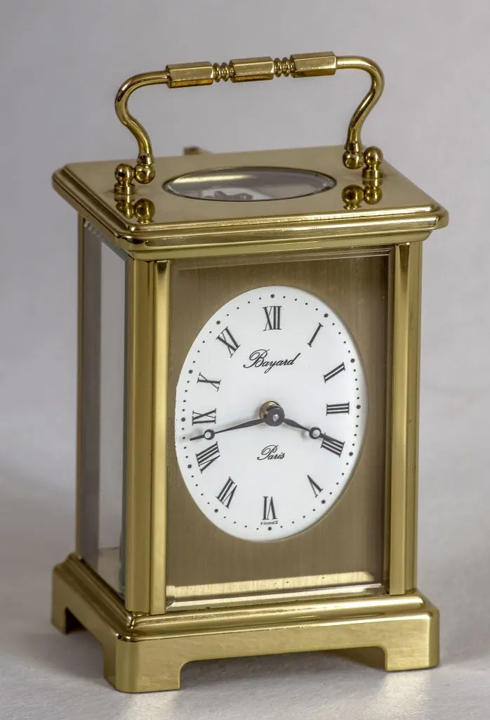 Pendulette de voyage en laiton poli à poignée, vitrée sur quatre faces, cadran ovale blanc signé Bayard Paris