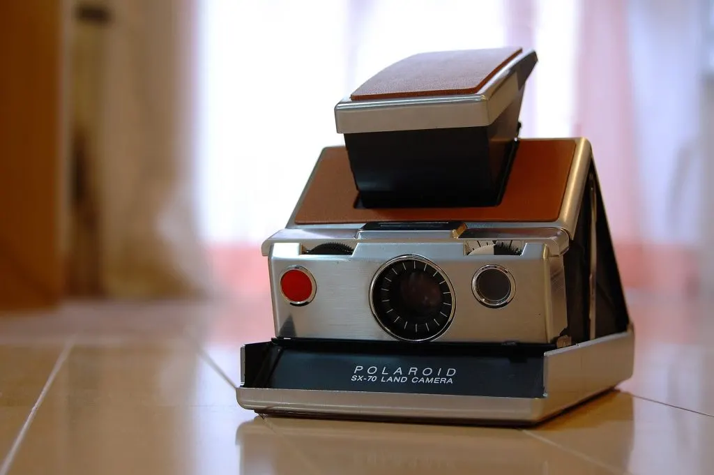 Polaroid SX-70 Land Camera pliant, gainé de cuir brun et chromé, posé sur un carrelage