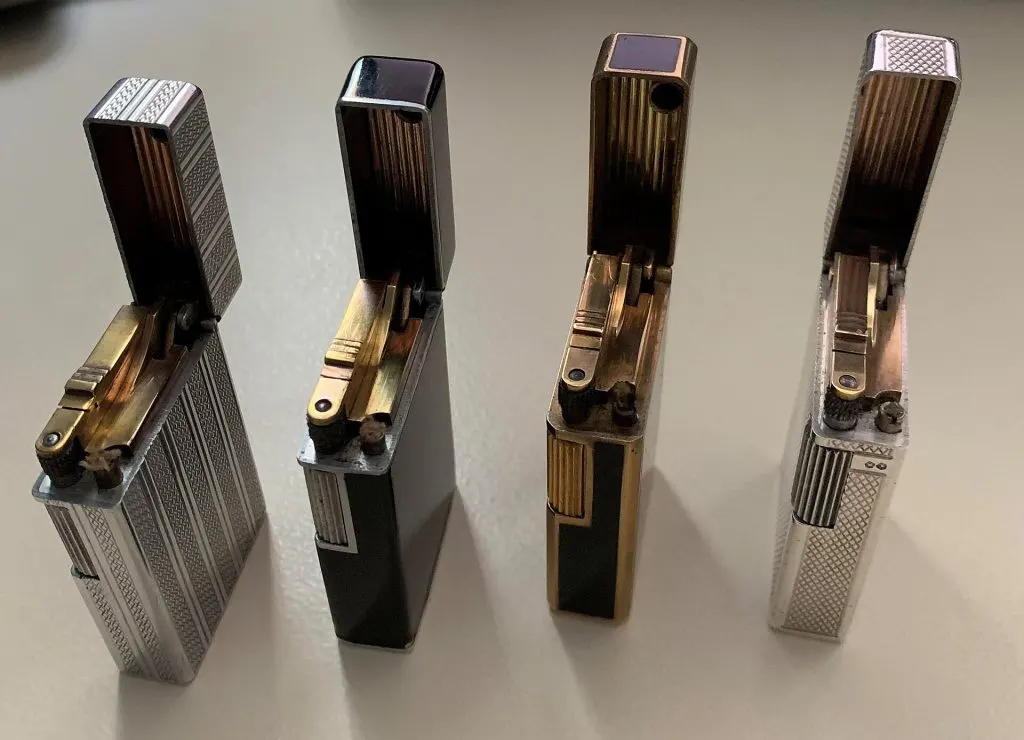 Quatre briquets S.T. Dupont à essence des années 1940, capots ouverts, en métal argenté, laqué et doré