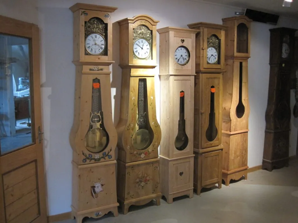 Rangée d'horloges comtoises à caisses en sapin, violonées ou droites, avec balanciers visibles
