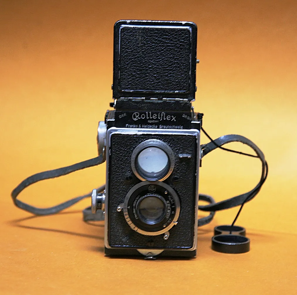 Rolleiflex noir à deux objectifs superposés avec capuchon de visée ouvert et courroie