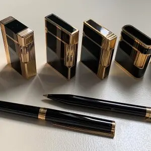 Six briquets S.T. Dupont plaqué or et laque de Chine noire alignés devant deux stylos assortis