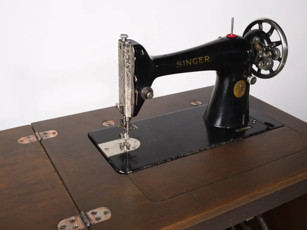 Tête noire d'une machine à coudre Singer 66K posée sur le plateau en bois de son meuble à pédale