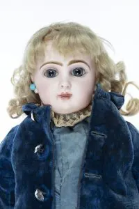 Visage d'une poupée Jumeau en biscuit vers 1890, yeux bleus en verre, perruque blonde et manteau de velours bleu